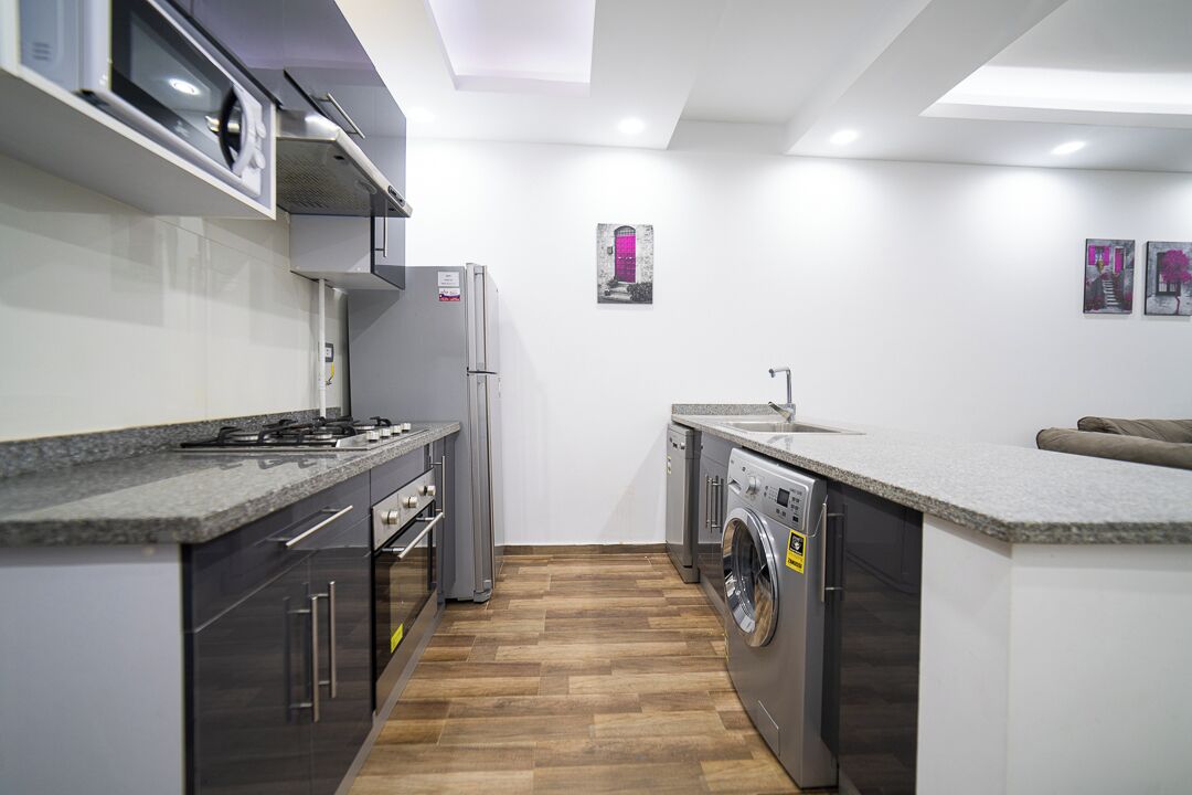 A compact kitchen with a built-in oven, microwave, and washing machine, a sink, and a small seating area.