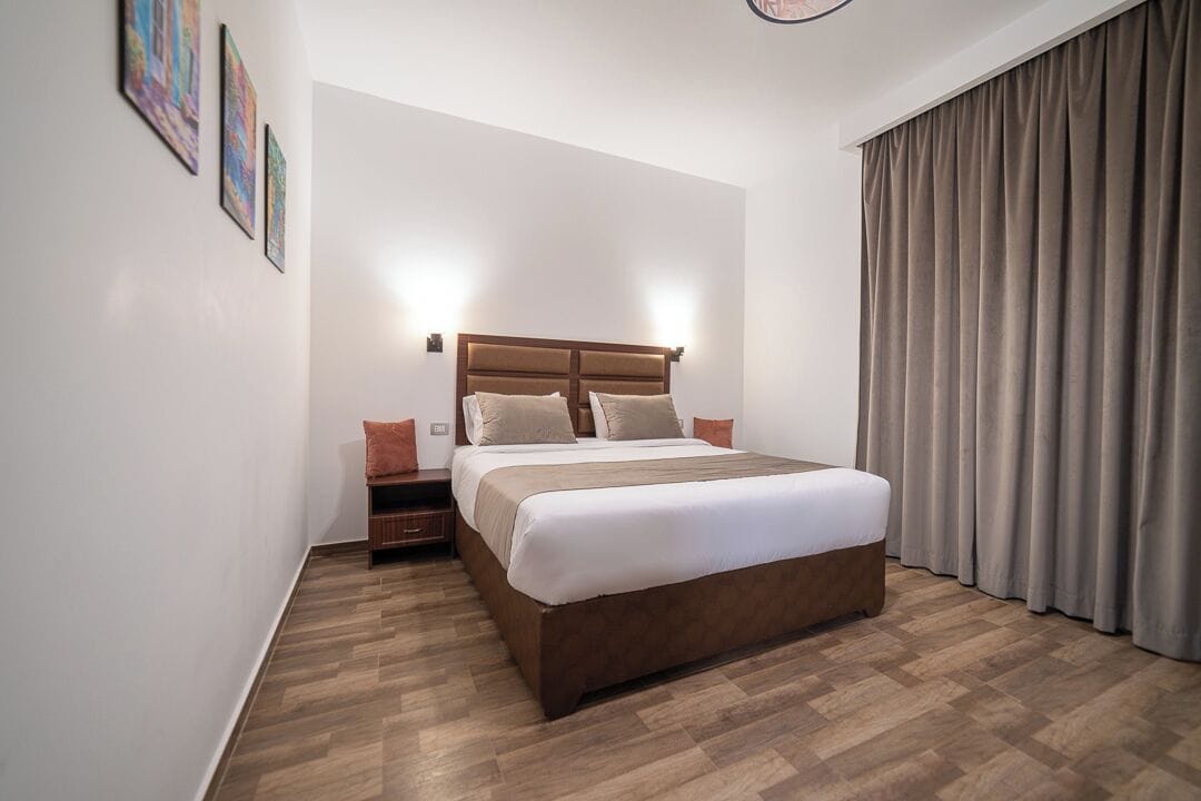 Une chambre à coucher bien rangée, avec un grand lit, une table de chevet et une lampe fixée au mur.