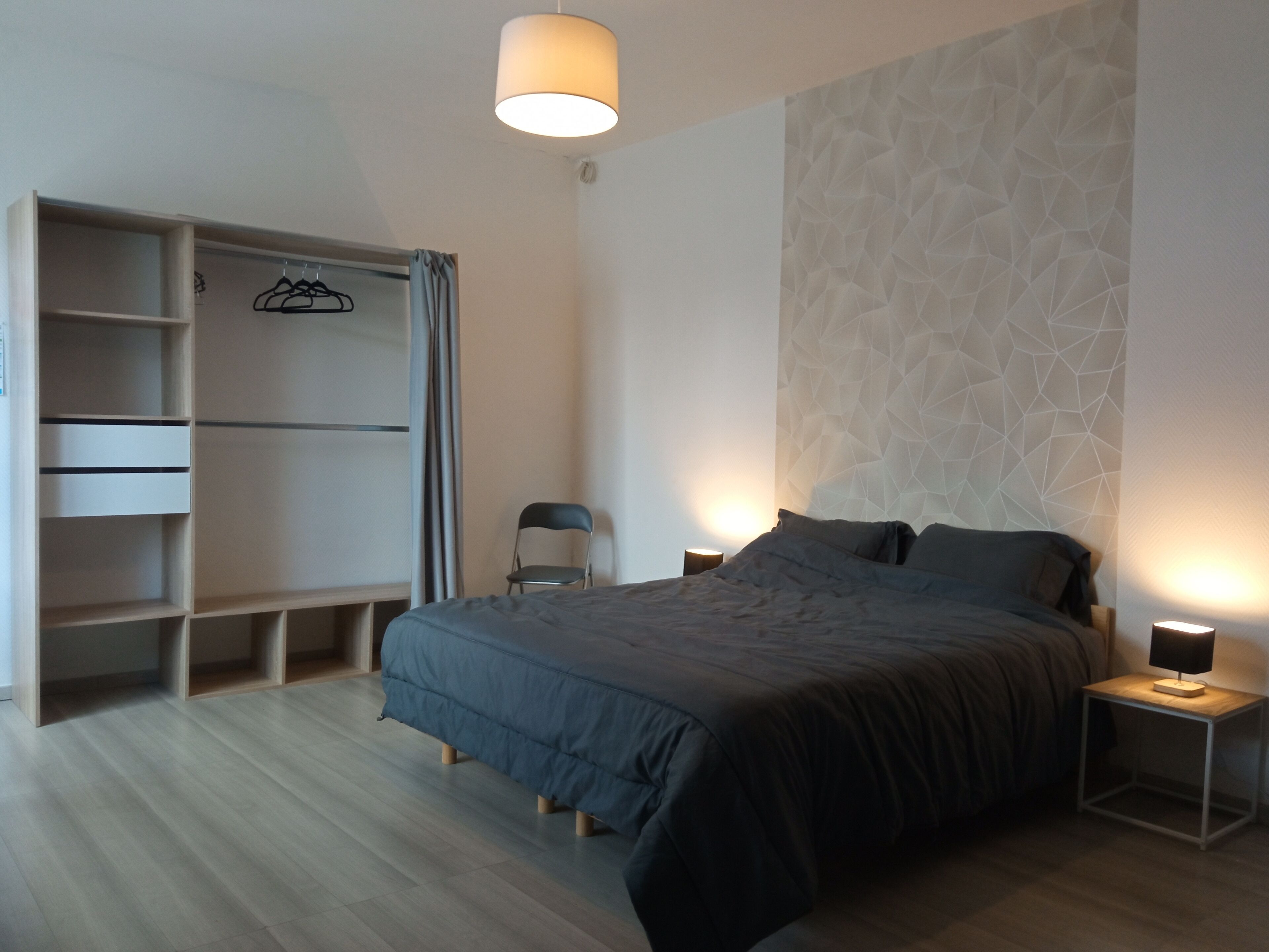 Een slaapkamer met een bed, nachtkastjes, een kledingkast en een stoel.