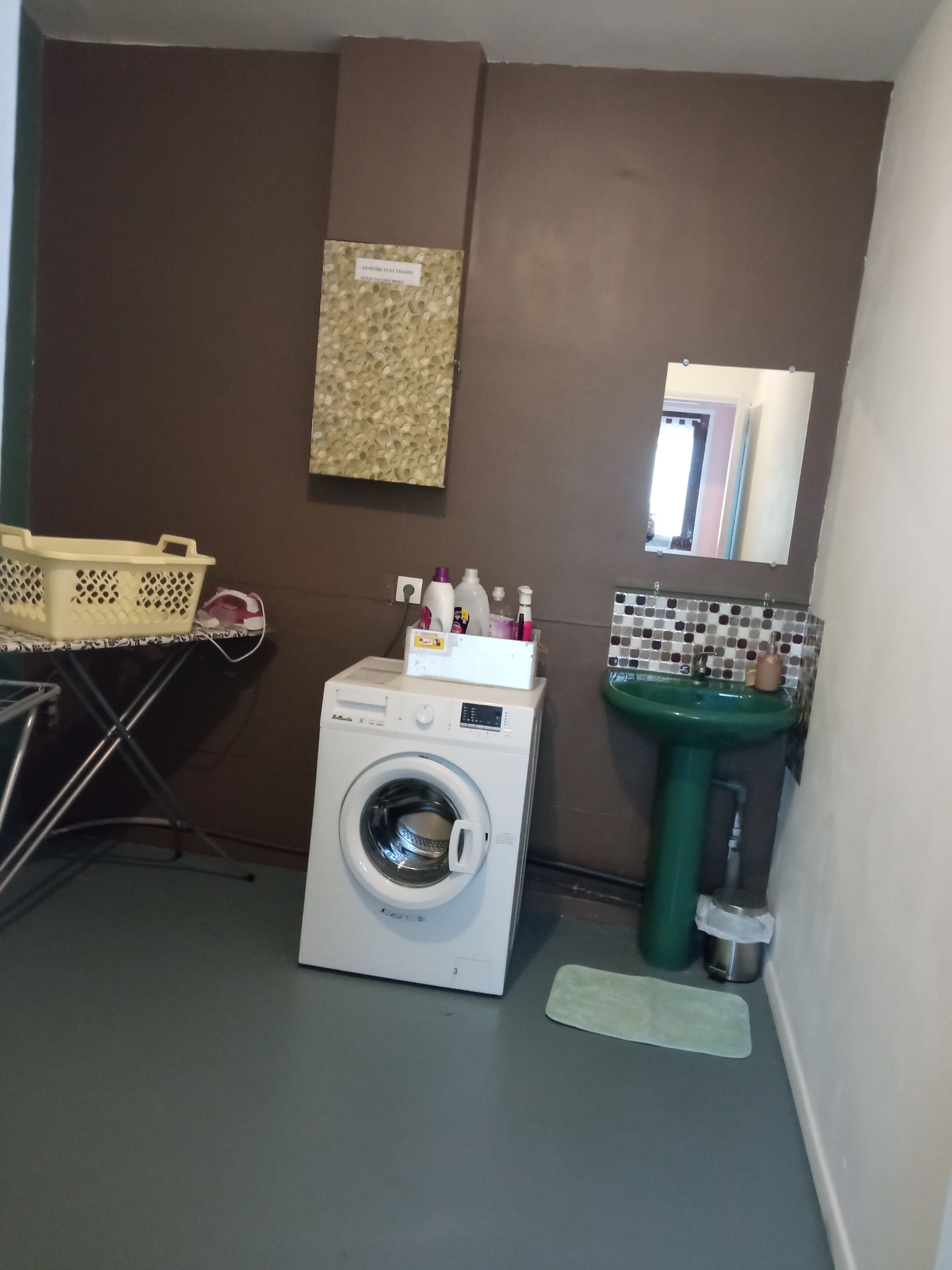 A compact laundry room with a front-loading washing machine, a green sink, and a small mirror above the sink.