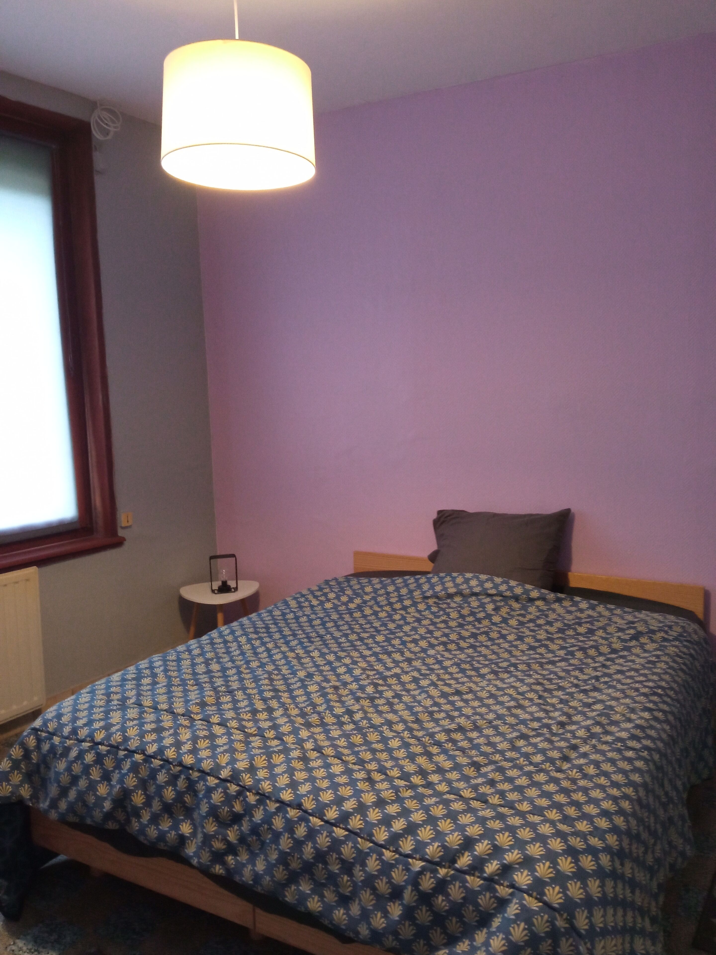 Une chambre à coucher avec un lit, une table de chevet, une lampe et une fenêtre.