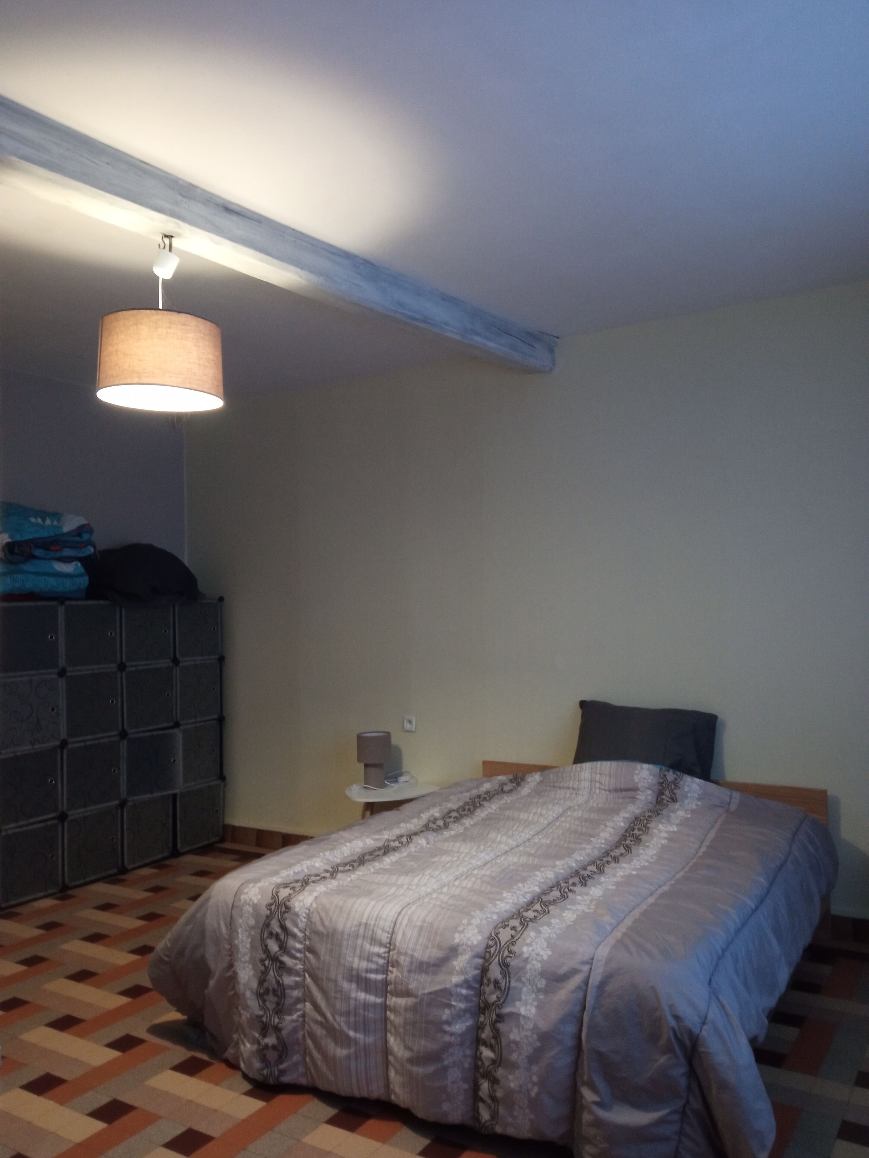 A bedroom with a bed, a dresser, a nightstand, and a hanging lamp.