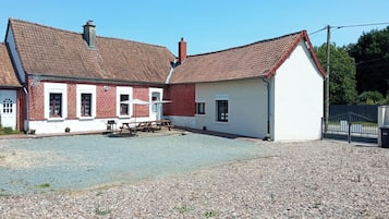 A two-story building with a red-tiled roof, a gravel driveway, and a fenced area.