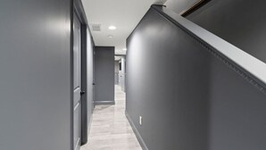 Un couloir aux murs gris et au plancher en bois, qui mène à une porte au fond.