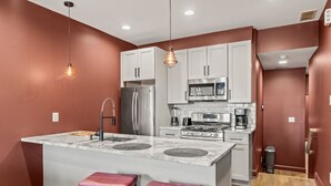 Une cuisine avec des meubles blancs, un îlot central doté de tabourets, des appareils en acier inoxydable et des luminaires suspendus.