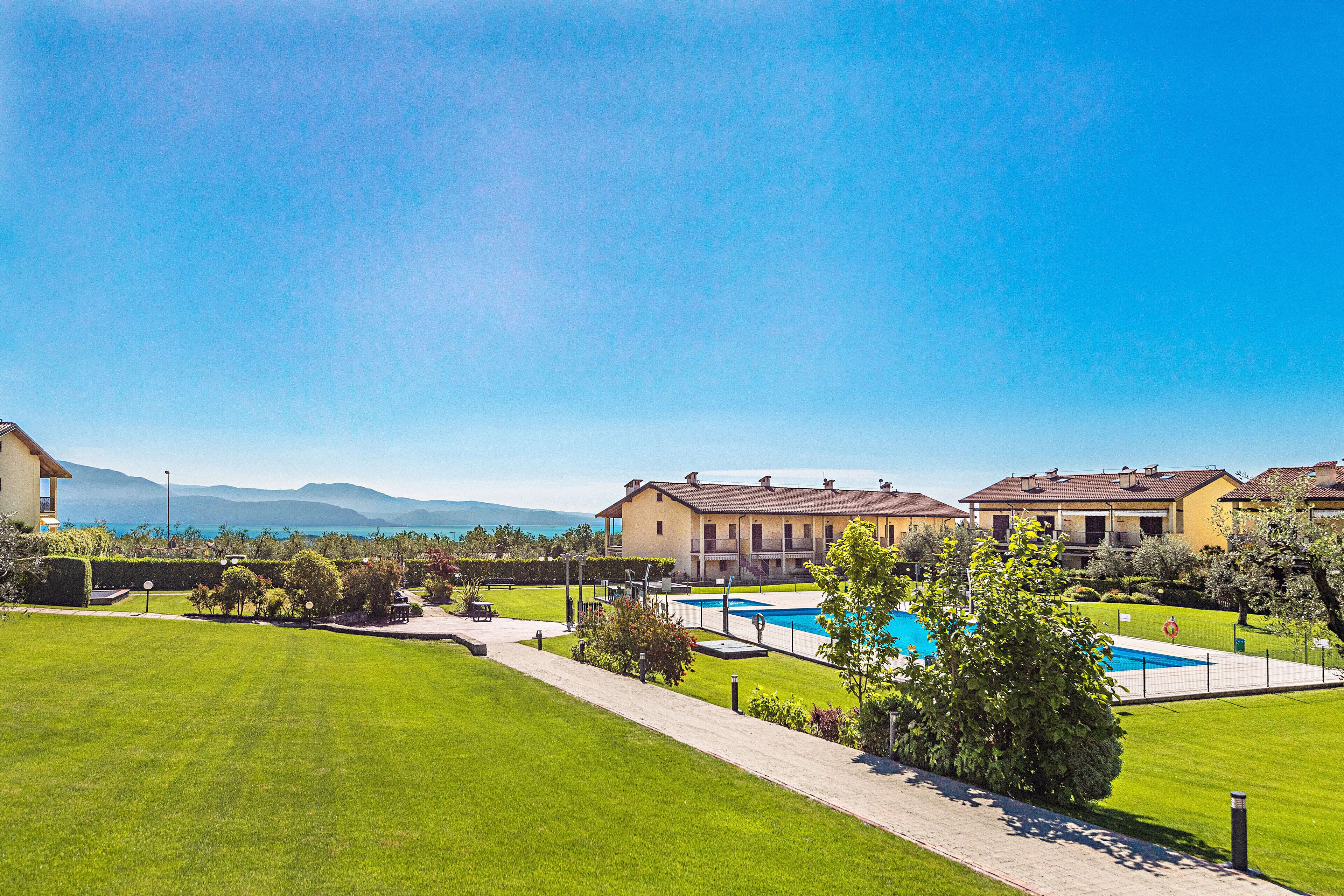 A residential area with a swimming pool, well-maintained lawns, and houses with balconies.