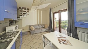 Eine kompakte Küche mit Gaskochfeld, Mikrowelle und blauen Schränken. Ein graues Sofa steht in der Nähe einer Glastür, die auf einen Balkon führt.