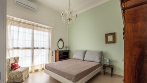 A bedroom with a bed, a chair, a nightstand, a lamp, a mirror, and a wooden wardrobe. - Appartamento a due passi da Villa Trabia by Wonderful Italy (Palermo)
