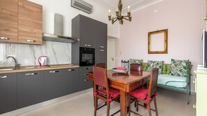 A modern kitchen with dark cabinets, a marble countertop, and a dining area with a wooden table and chairs. - Appartamento a due passi da Villa Trabia by Wonderful Italy (Palermo)