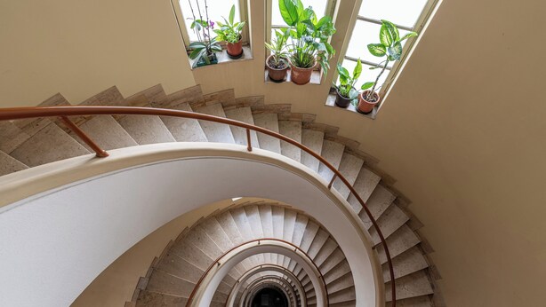 A spiral staircase with a curved handrail, flanked by potted plants on windowsills. - Appartamento a due passi da Villa Trabia by Wonderful Italy (Palermo)