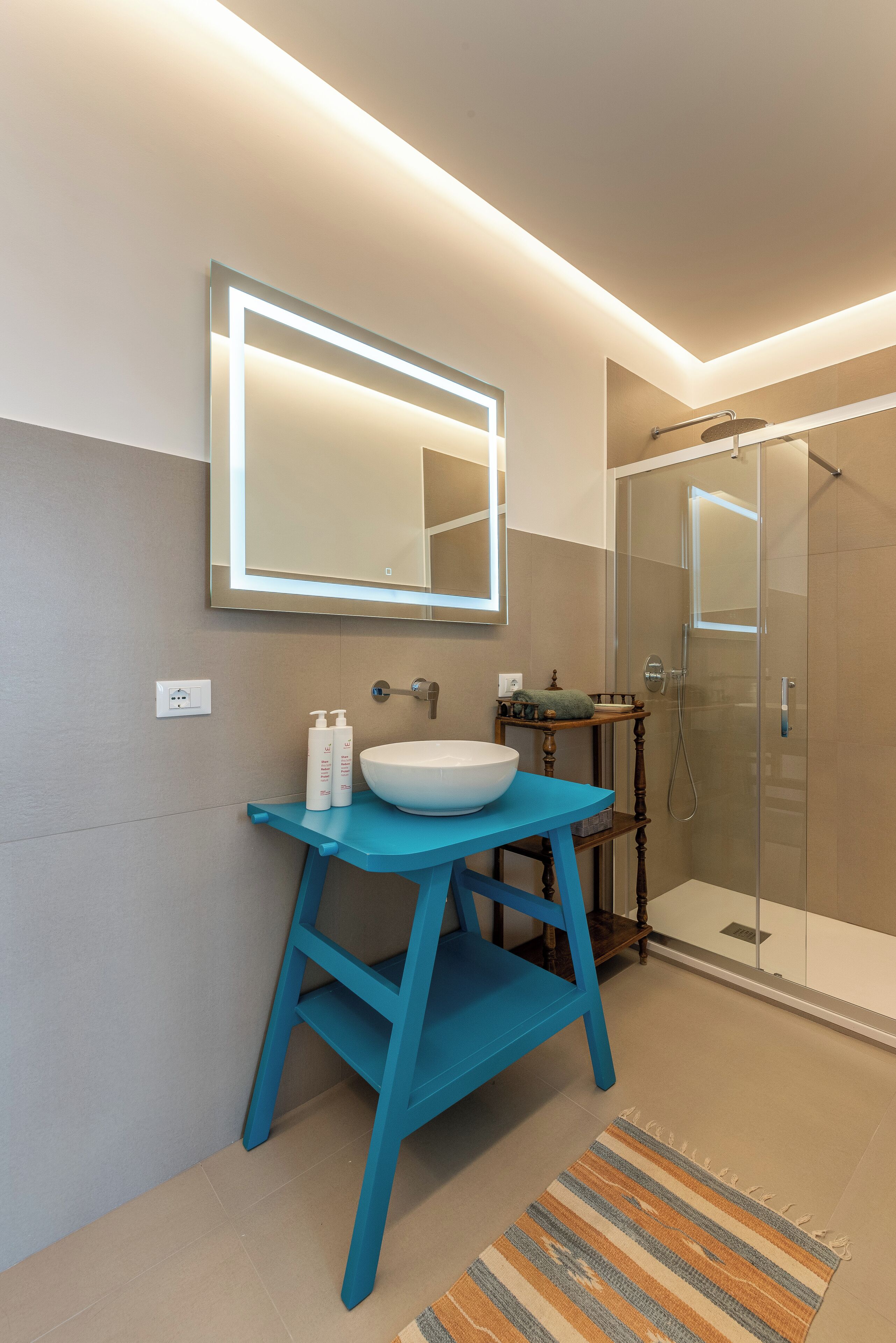 A modern bathroom with a blue vanity, a large mirror, and a glass-enclosed shower.