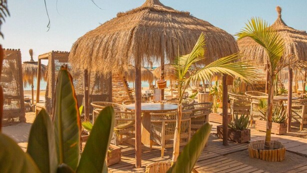 Ein Restaurant direkt am Strand mit Reetdachschirmen, Korbmöbeln und einer Holzterrasse.
