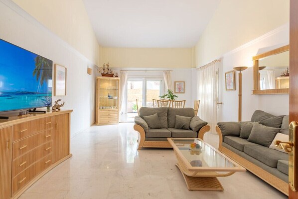 Un salón amplio con un televisor de pantalla plana grande, dos sofás, una mesa de centro de vidrio y un mueble de madera.