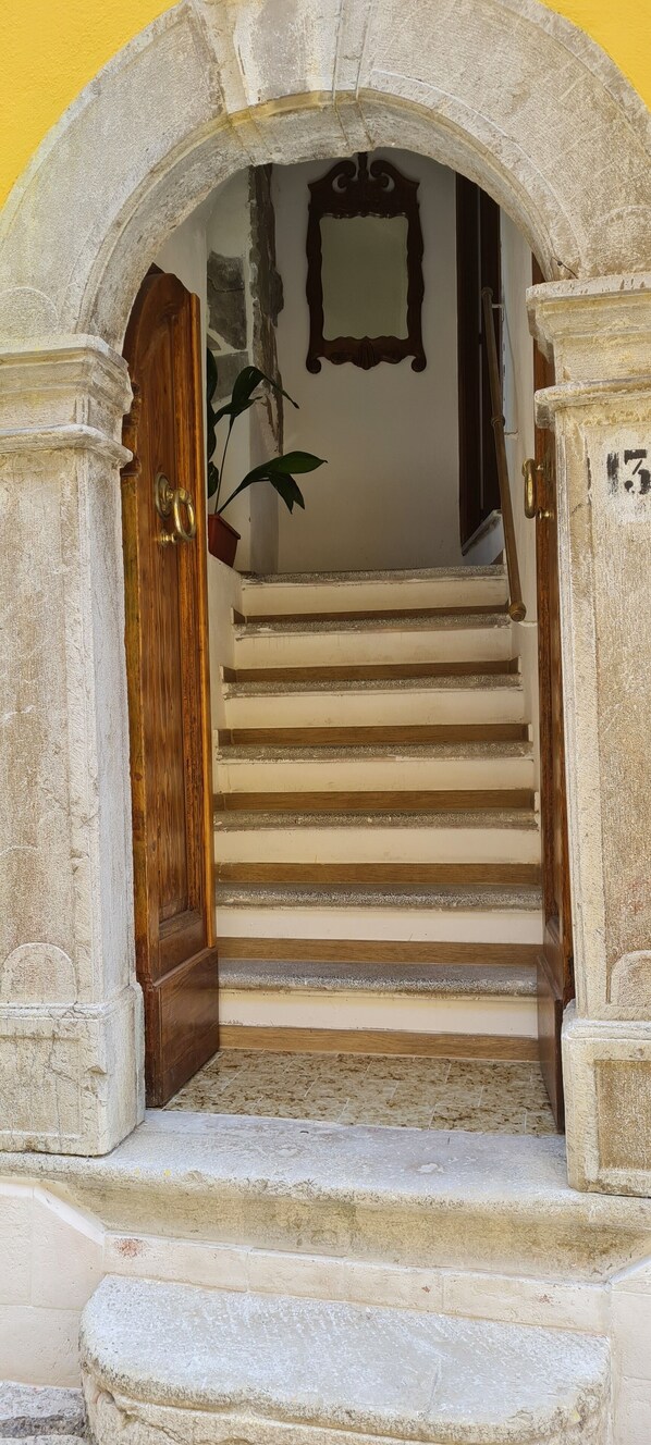 Un arco de piedra que da paso a una escalera con una puerta de madera y una planta en maceta.