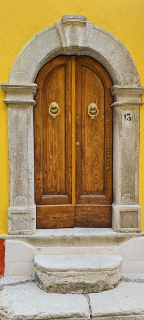 Una puerta doble de madera con un arco de piedra, sobre un muro amarillo.