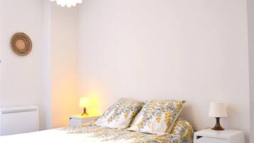 A bedroom with a bed, two bedside tables, a lamp on each table, a wall-mounted light fixture, and a decorative wall hanging.