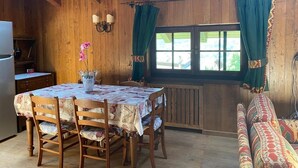 A wooden cabin interior with a dining table, chairs, a sofa, and a window with curtains. - Espoire cir 0025 (La Salle)