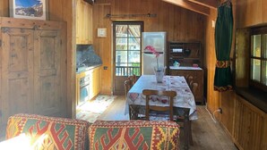 A cozy cabin interior with a dining table, chairs, a refrigerator, and a window with curtains. - Espoire cir 0025 (La Salle)