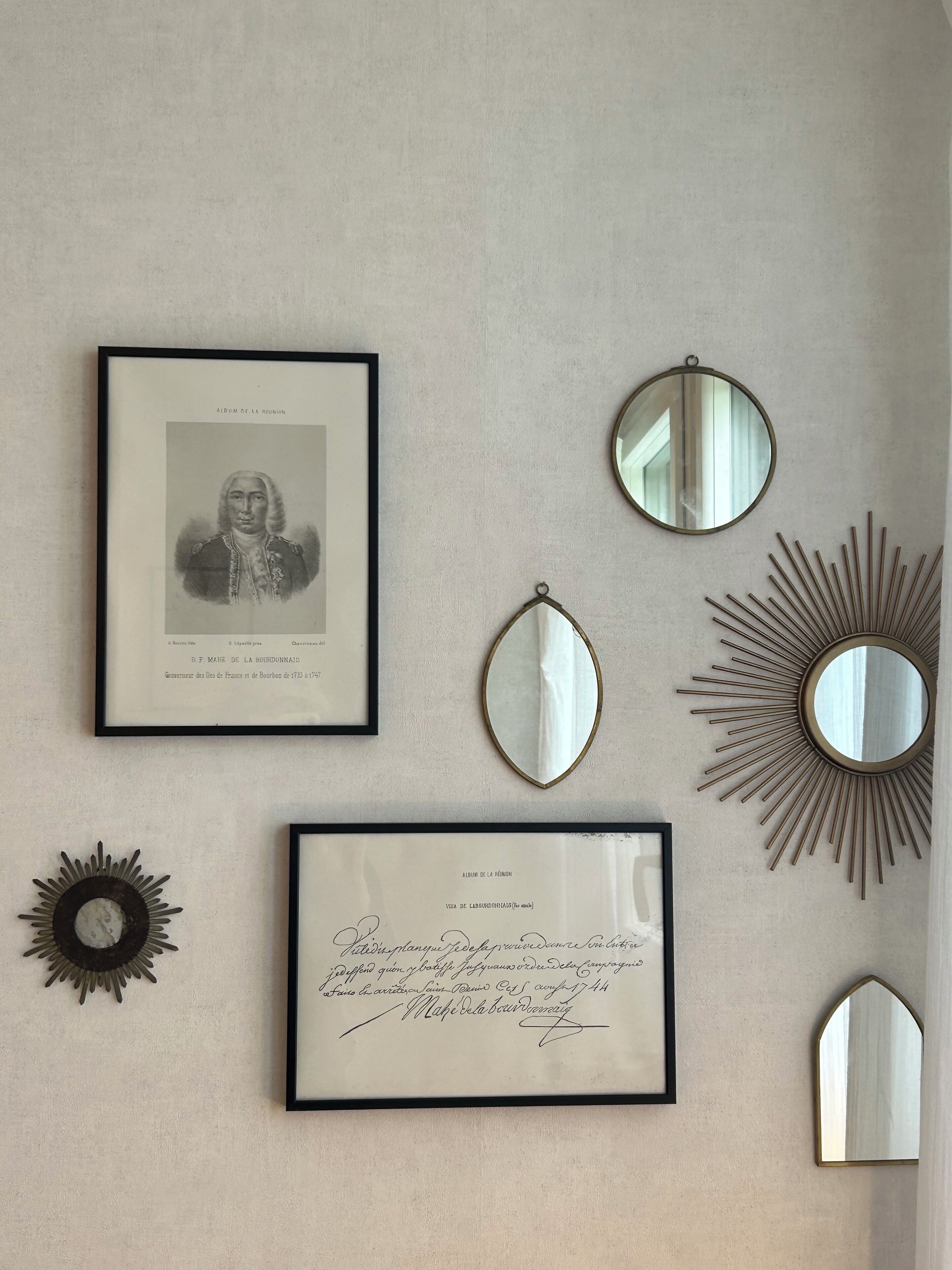 A wall with various framed items, including a portrait, a certificate, and decorative mirrors.