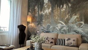 Un soggiorno con un tavolino in legno, un divano con cuscini decorati, un grande murale raffigurante una foresta e una lampada da terra alta.