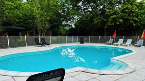 Una piscina con piso de baldosas, rodeada por una cerca, equipada con sillas de descanso y sombrillas.