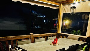Un área de comedor al aire libre con mesa y sillas, vista al cielo nocturno y barandilla de madera.