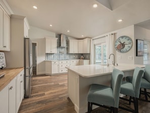 A modern kitchen with white cabinetry, a central island with bar seating, and a decorative clock on the wall. - Island Vibes Beach House~ 4 min. Walk 2 Beach • Heated Pool • King Beds (Melbourne Beach)