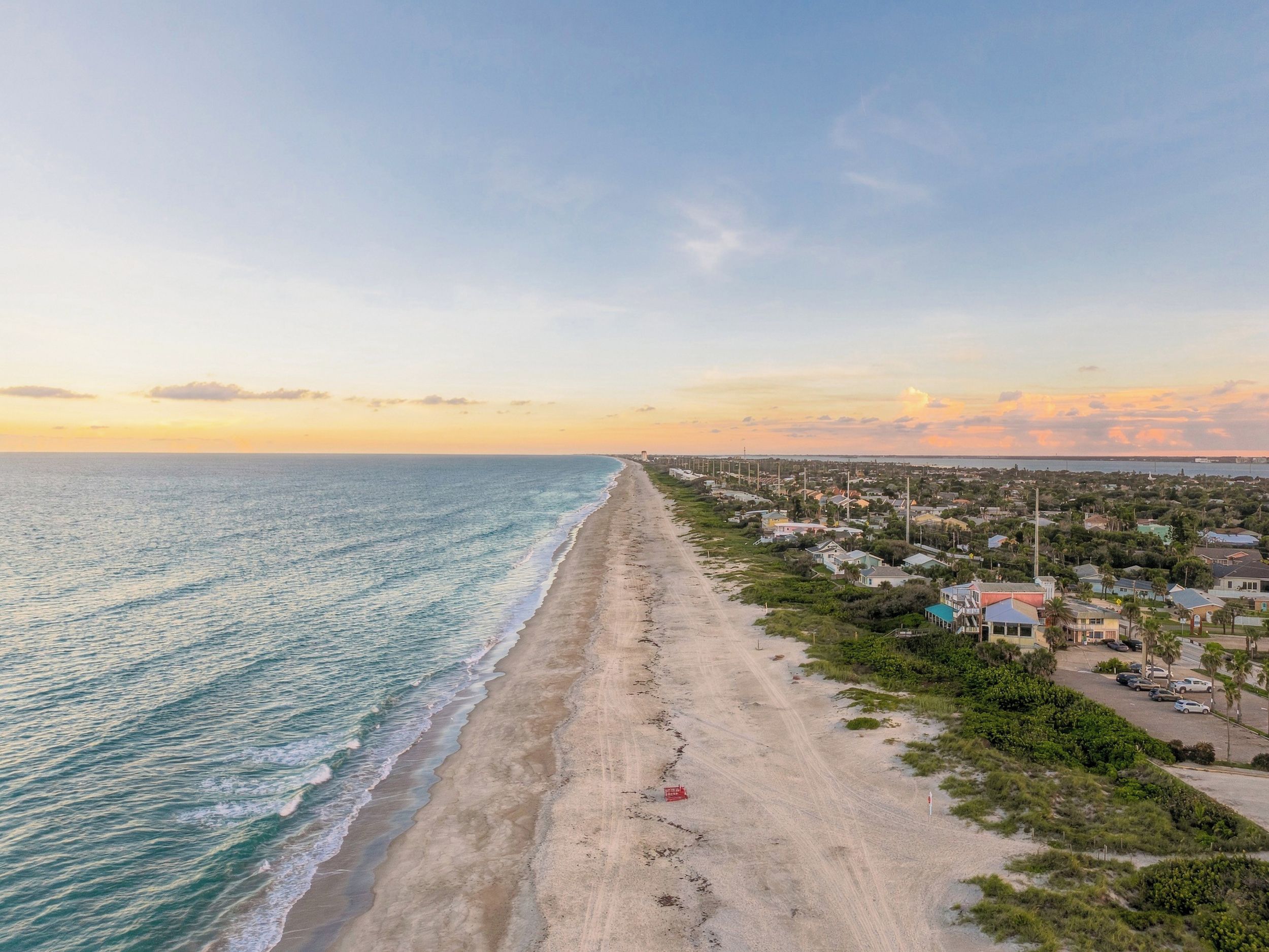 A coastal road with a beach on one side and a residential area on the other.