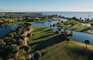 Eine Vogelperspektive auf einen Golfplatz mit mehreren Wasserhindernissen und einem großen Gewässer im Hintergrund.