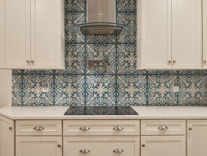 A kitchen with white cabinets, a stainless steel range hood, and decorative blue and white tiles.