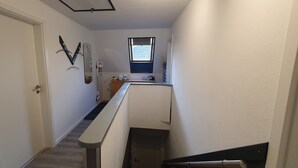 Passadís estret amb una porta blanca, un petit finestral i un mirall a la paret.