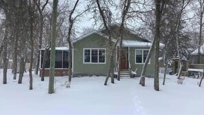 Une maison de plain-pied avec un porche à l’avant, entourée d’arbres couverts de neige.