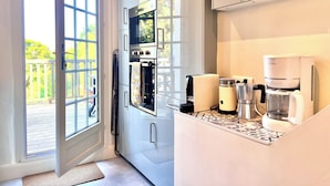 Eine moderne Küche mit Backofen, einer Kaffeemaschine und Blick ins Freie durch eine Glastür.