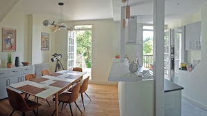 Eine moderne Küche mit einer zentralen Kochinsel, einem Essbereich mit einem langen Tisch und Stühlen, sowie einem großen Fenster, das für natürliches Licht sorgt.