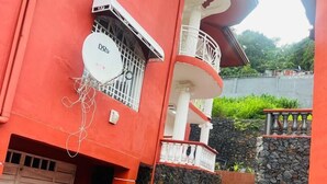 A red building with a white balcony, a satellite dish, and a stone wall. - Mountains View Villa  (Freetown)