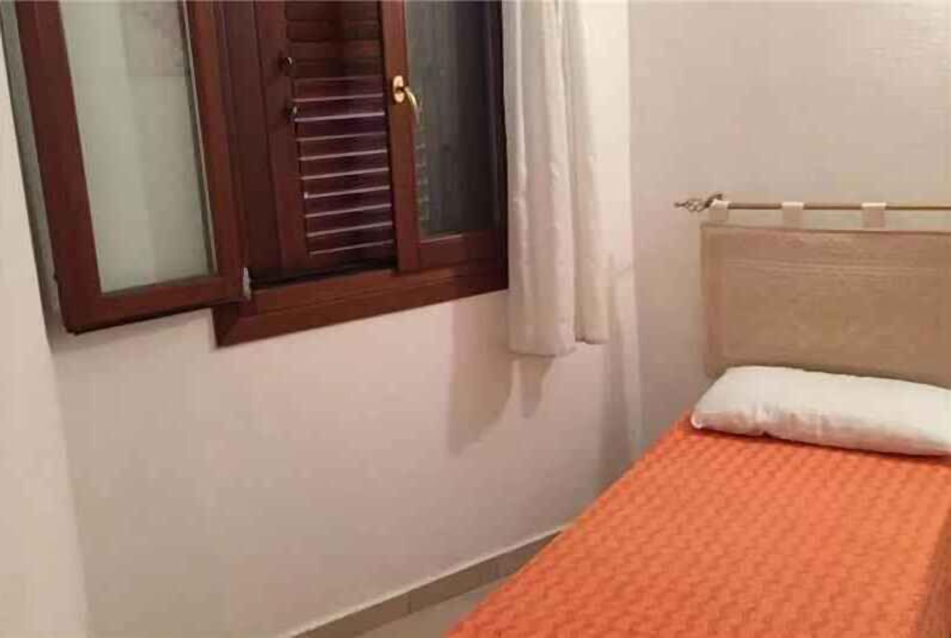 A bedroom with a bed, a window with blinds, and a radiator.