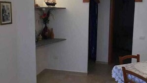 Una habitación pequeña con una cama, una silla, un estante con adornos y una puerta que da a otra habitación.