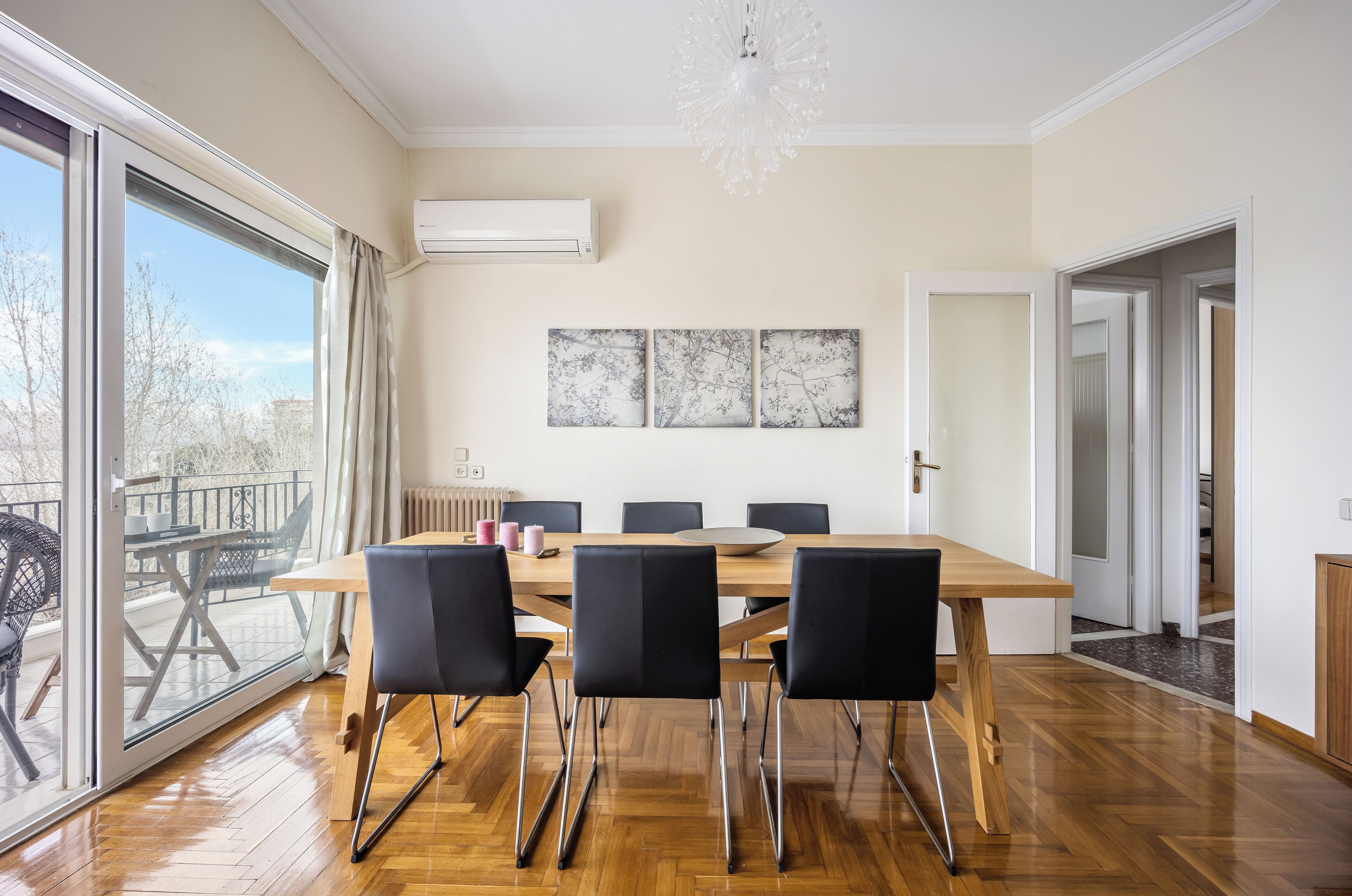 Comedor moderno con una mesa de madera y sillas negras, ventanas amplias con vistas y una araña.