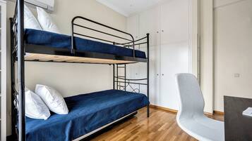 A bunk bed room with a desk and chair, white walls, and wooden flooring.