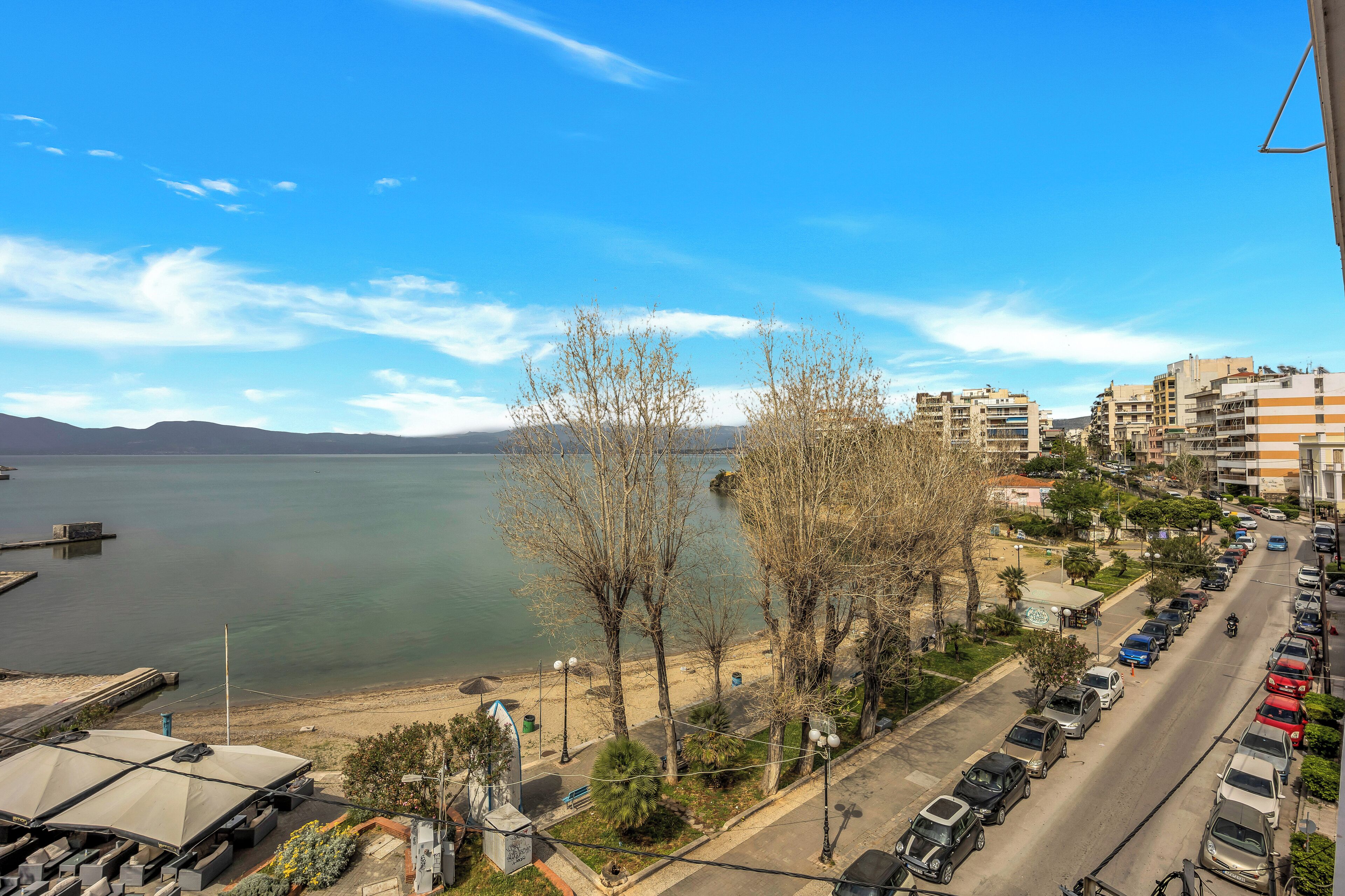 Un paysage urbain côtier avec un port de plaisance, des voitures garées et des bâtiments le long du front de mer.