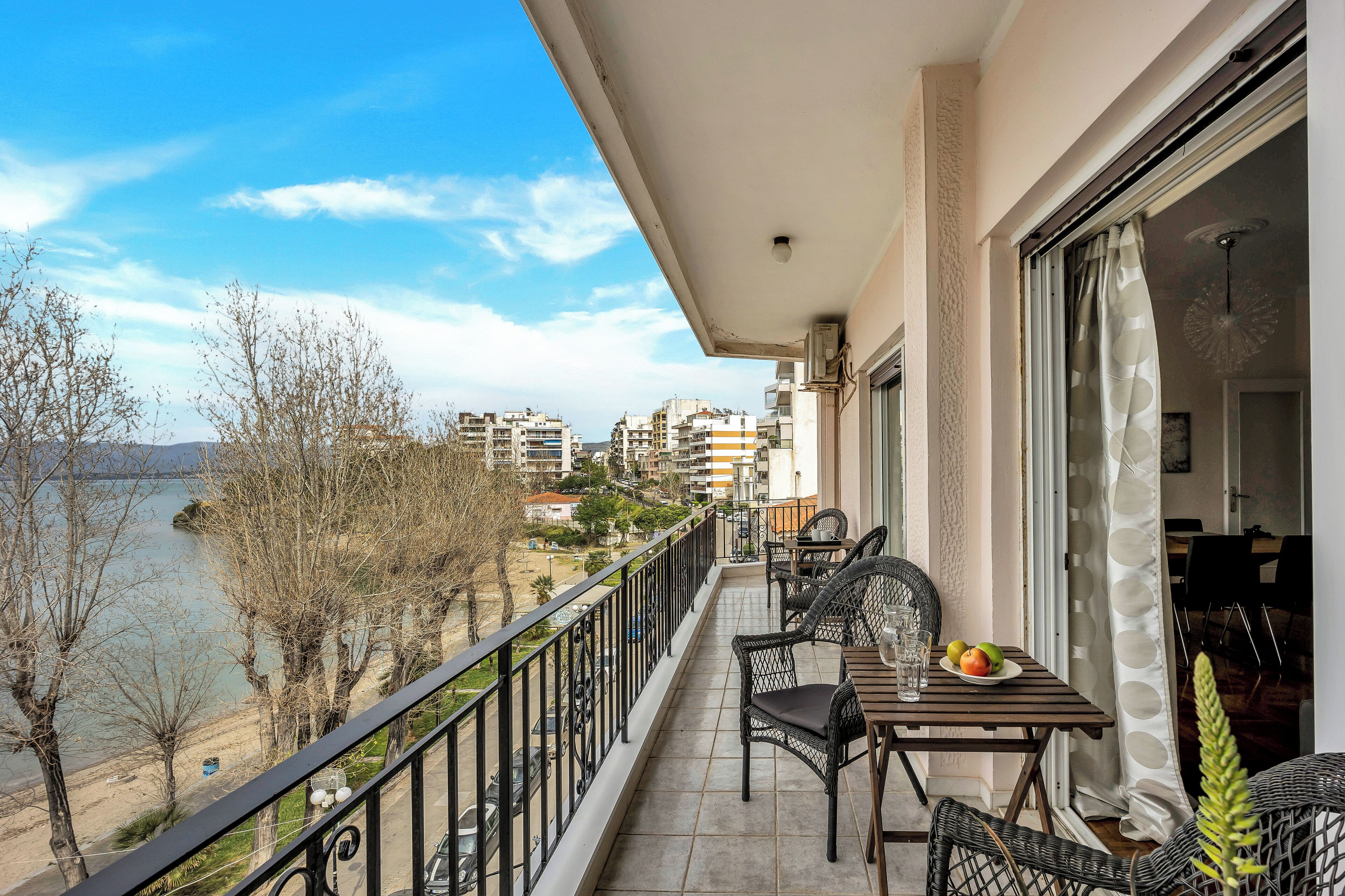 Un balcon avec une table et des chaises, donnant sur une étendue d’eau et des bâtiments.