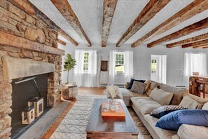 Ein gemütliches Wohnzimmer mit freiliegenden Holzbalken, einem Kamin aus Stein und einem bequemen Sofa.