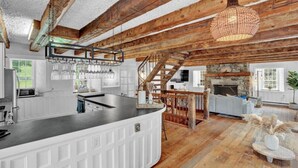 Une cuisine rustique avec un plafond en bois, une cheminée en pierre et un coin repas agrémenté d’un escalier.