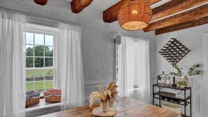Un coin repas rustique avec une table en bois, des rideaux blancs et un lustre en osier.
