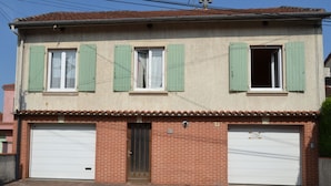Un bâtiment à deux étages avec des volets verts, une façade en briques et deux portes de garage.