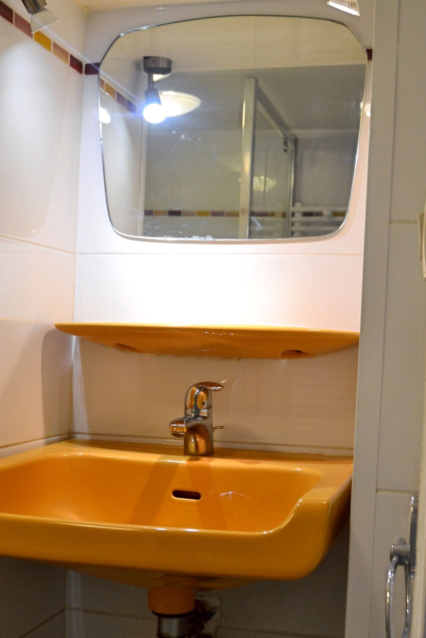 A bathroom with a yellow sink, a mirror above it, and a shower area visible through the glass door.