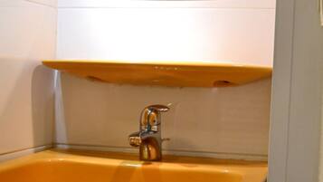 A bathroom with a yellow sink, a mirror above it, and a shower area visible through the glass door.