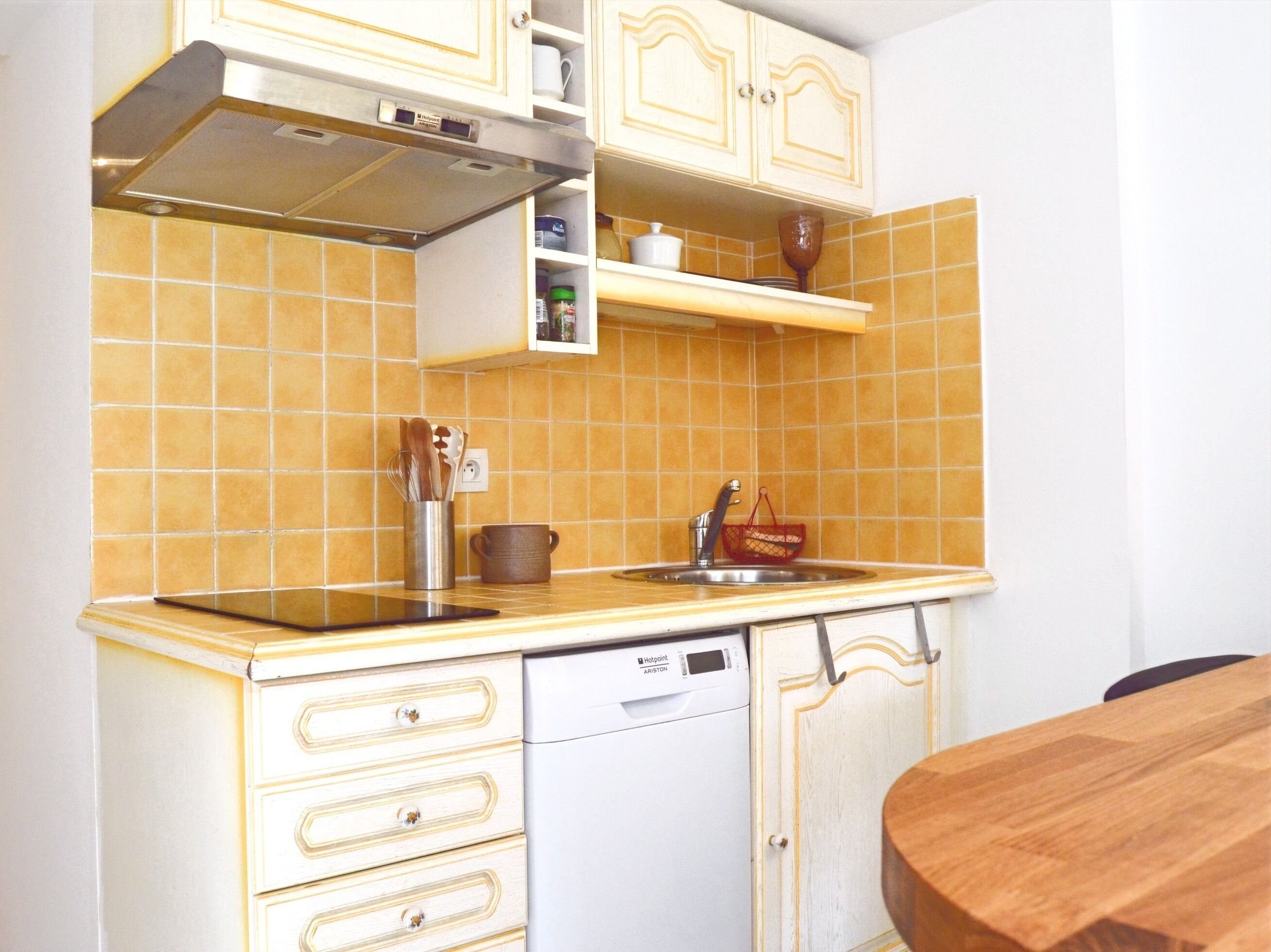 Een compacte keuken met een vaatwasser, een spoelbak en een magnetron. Er zijn kastjes boven het aanrecht en een klein plankje met een beker en een pot.