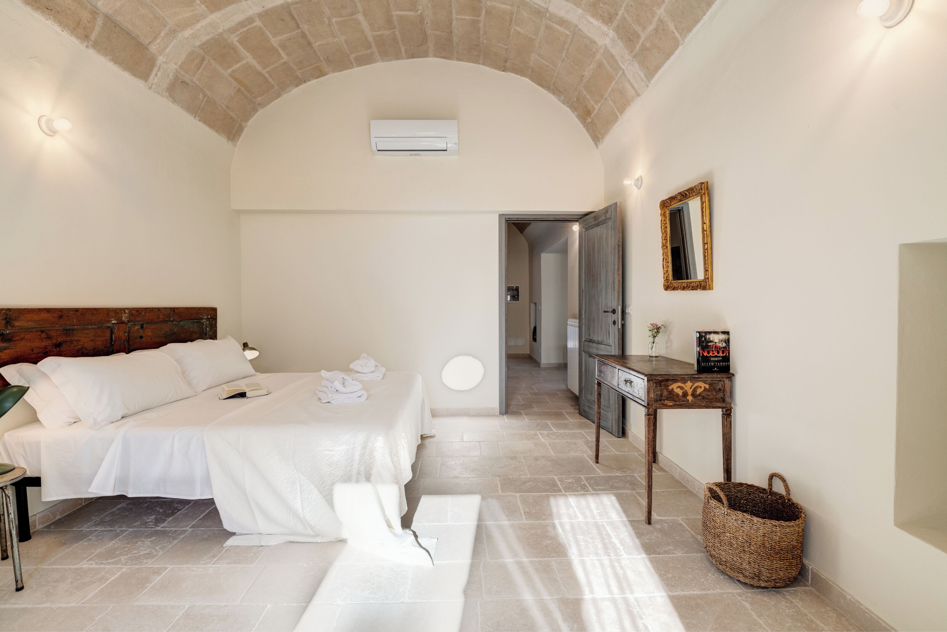 Un dormitorio con una cama grande, cabecera de madera, mesita de noche, espejo y aire acondicionado de pared.