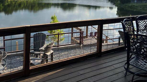 Una terraza de madera con sillas que da a un lago tranquilo, rodeada de un bosque frondoso.